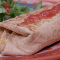 A grilled burrito topped with salsa and a green salad with tomato served on a multicolored plate.