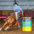 A man on a horse leans as they race around a colorful barrel.  