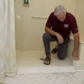 A man kneels in a walk-in shower, reaching down to a point in the entryway.