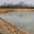 A partially filled pond with minimal plant life visible around the banks.