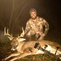 A man wearing hunting gear displays a deer he harvested with a bow and arrow.