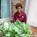 A woman sits on a patio behind a container where greens are growing.