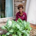 A woman kneels behind a planter on a brick patio.