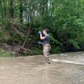 Woman in wading pants collects a water sample in a creek.