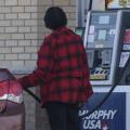 An adult pumps gas into a car at a gas station.