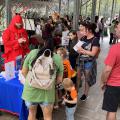 Several adults and children gather around an educational booth hosted by a man in a crawfish suit.