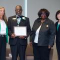 Four people stand in a line for a plaque presentation.