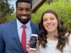 A smiling couple holds a smart phone showing a woman on a video call.