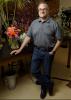 A man rests his hand on a table displaying floral arrangements.