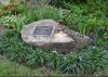 A stone with a plaque is surrounded by flowers in a garden.