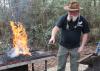 A man points at hot metal he just heated in a fire to forge it.