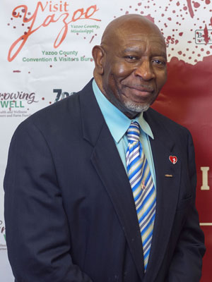 A man wearing a suit with a heart on the lapel stands in front of the Mississippi State University Extension Service logo.